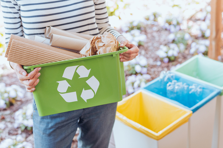 Person holding green recycling bin filled with cardboard and paper for proper waste sorting