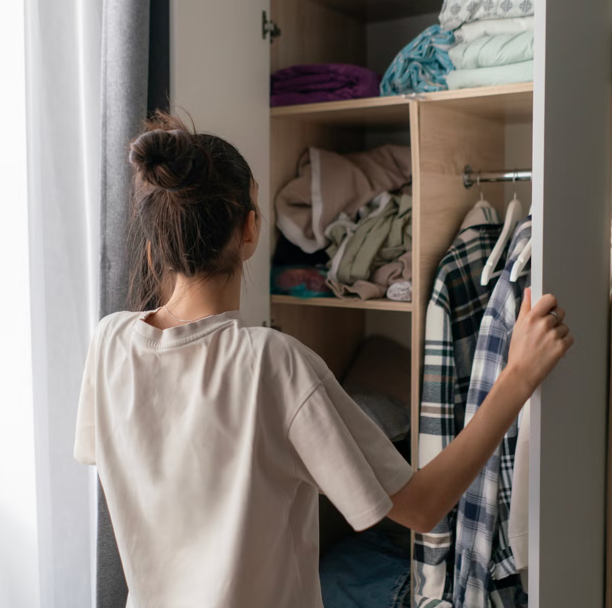 woman organizing clothes in wardrobe closet while decluttering bedroom storage