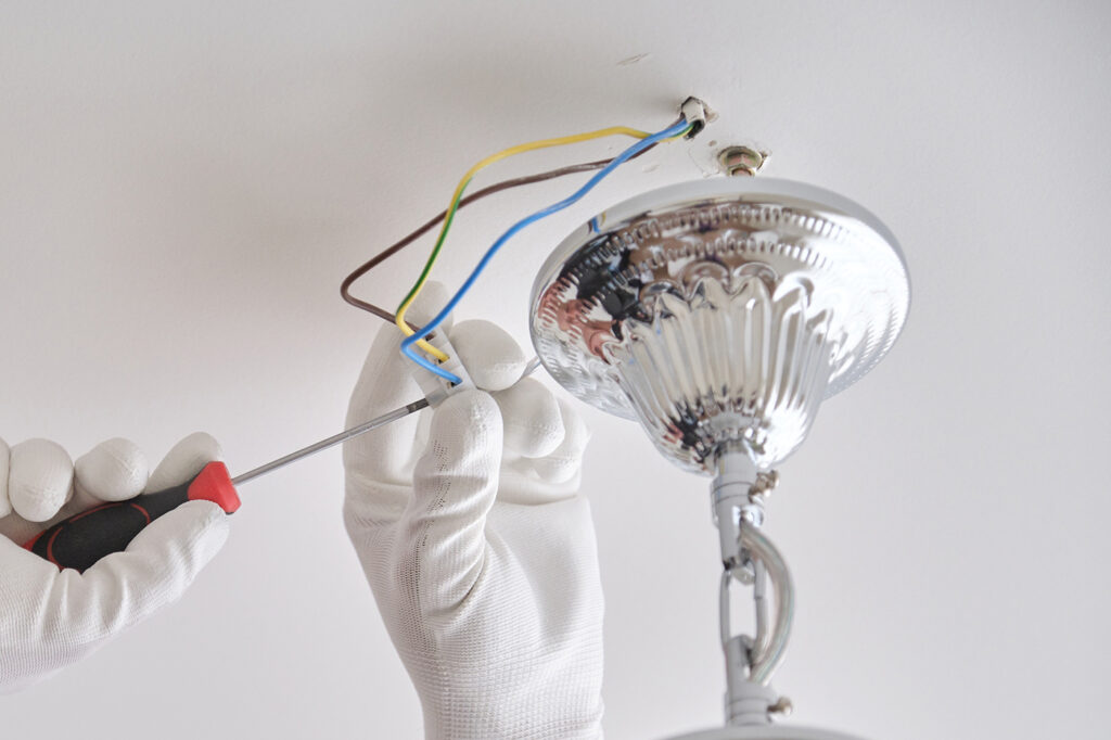 installing ceiling light fixture with screwdriver and exposed electrical wires