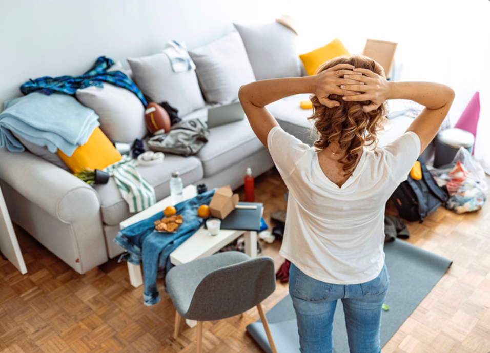 woman standing in a messy living room feeling overwhelmed by household clutter