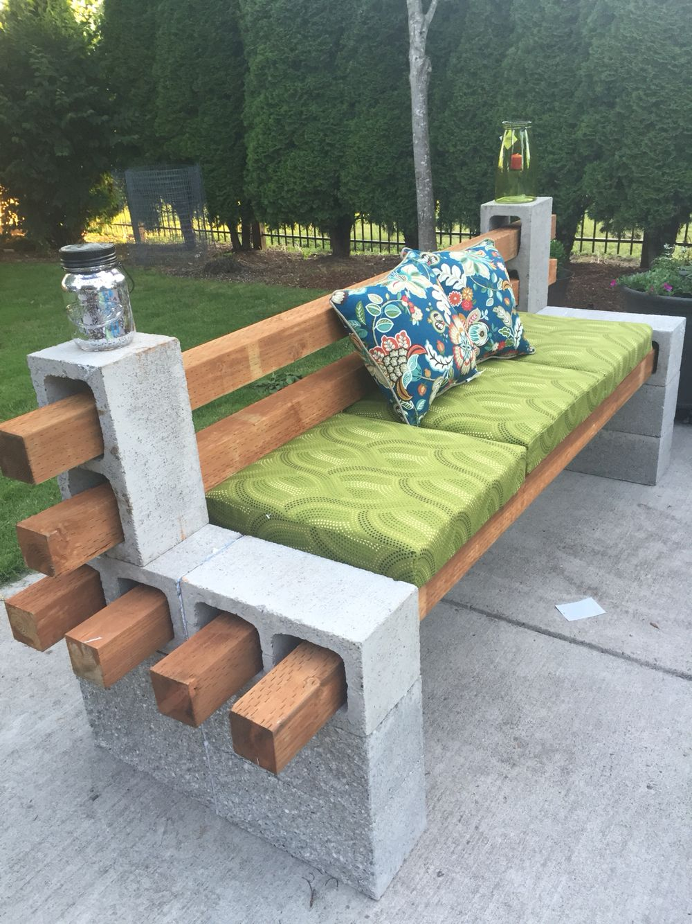 DIY cinder block and wood outdoor bench with green cushion for backyard seating