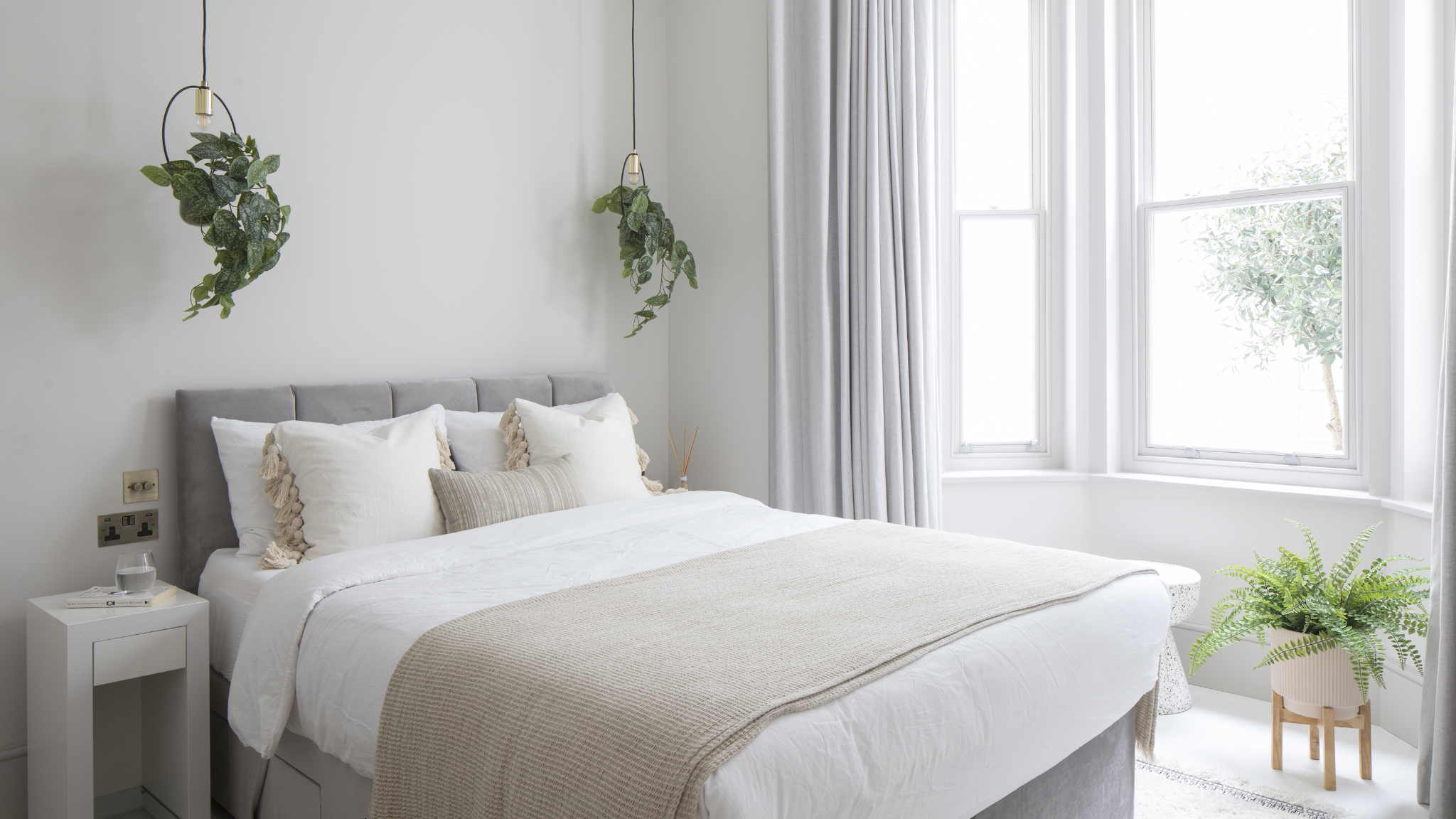 Bright minimal bedroom with white bedding and hanging plants