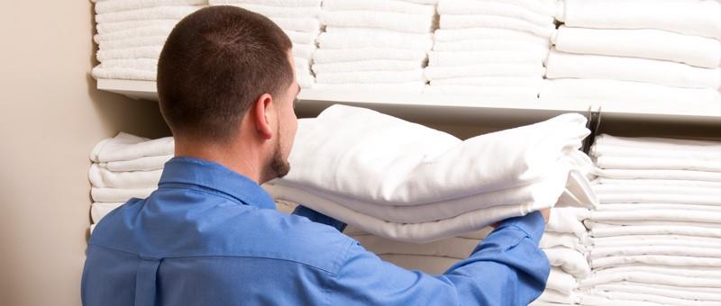 Man organizing white linens on a shelf.