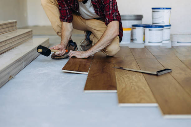 Person installing wooden flooring with rubber mallet and planks
