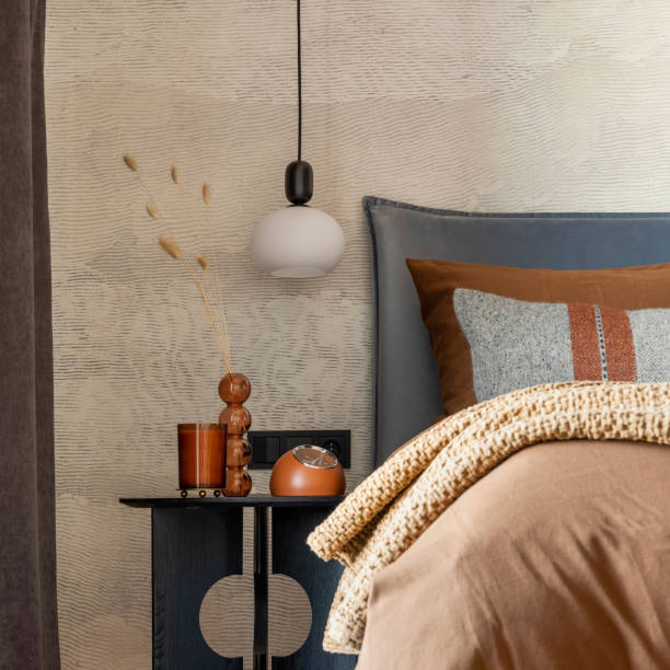 Stylish composition of modern bedroom interior. Bed, creative lamp and elegant personal accessories. Concrete wall. Brown sheets.