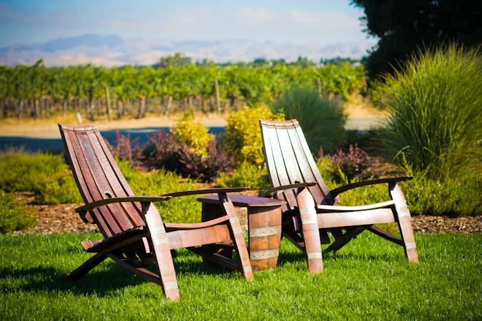 Two Adirondack chairs made from wine barrels on a lush lawn