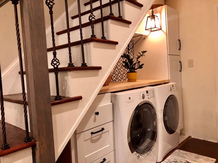 A washer-dryer set tucked under a home's stairwell with storage and lighting,