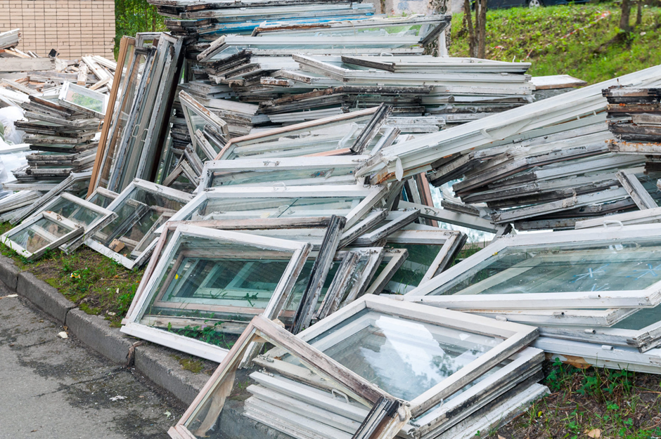 Piles of discarded window frames with weathered wood stacked near a building.