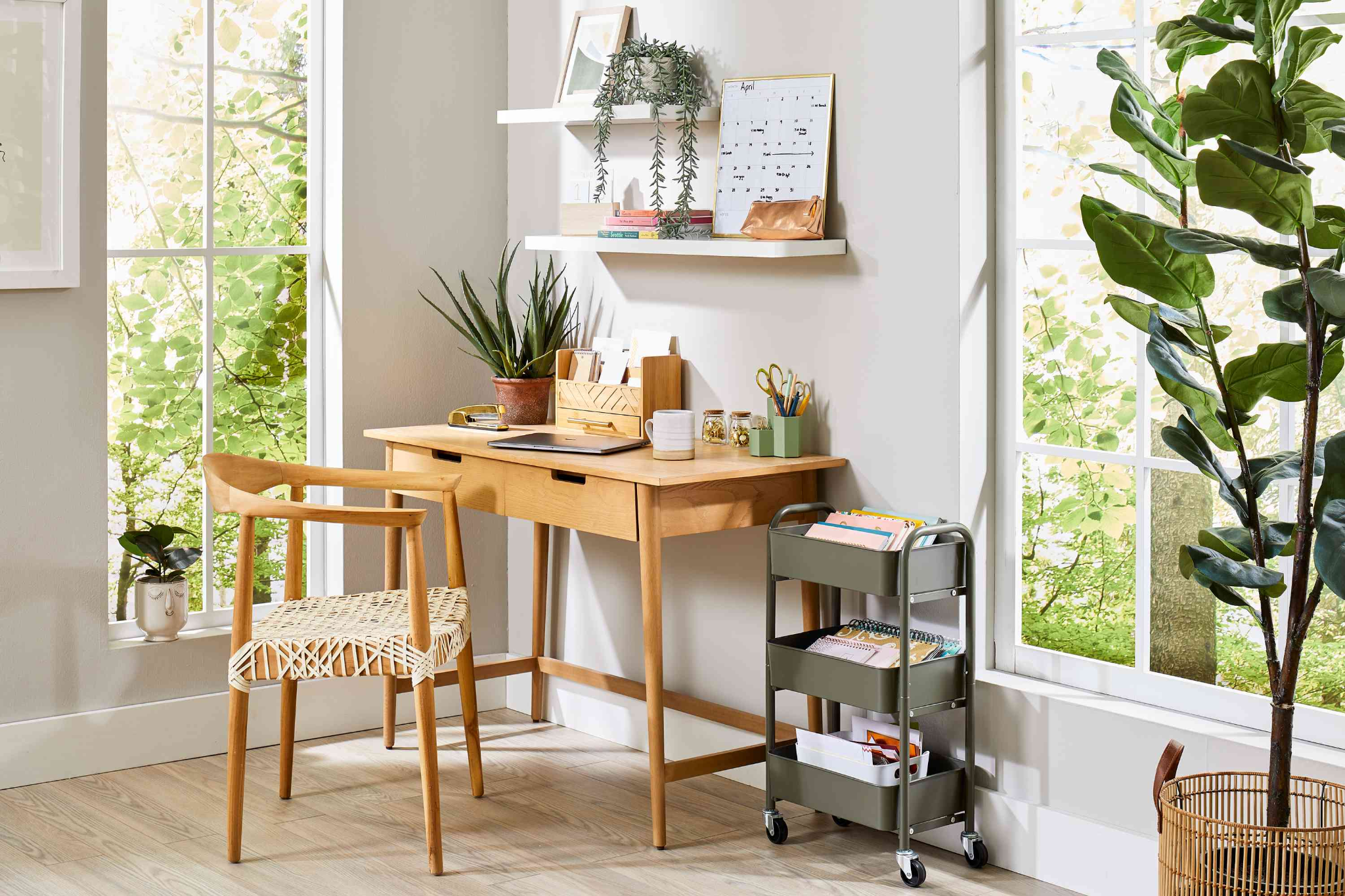 Minimalist wooden desk setup in a bright home office with plants and a rolling storage cart.