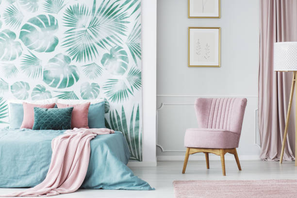 Pastel bedroom with pink chair and tropical leaf accent wall