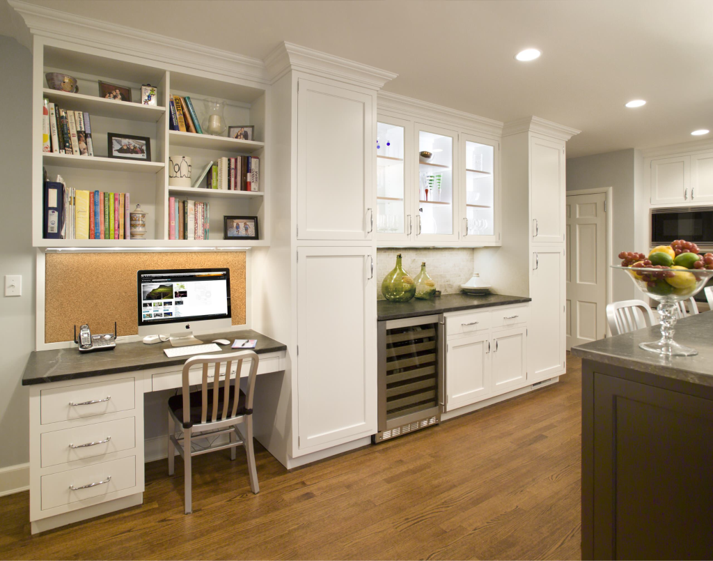 Home office built into kitchen cabinetry with white shelves and computer desk