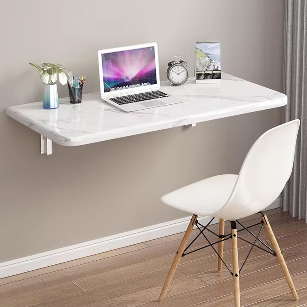 Wall-mounted foldable desk with a laptop and clock in a small modern workspace.