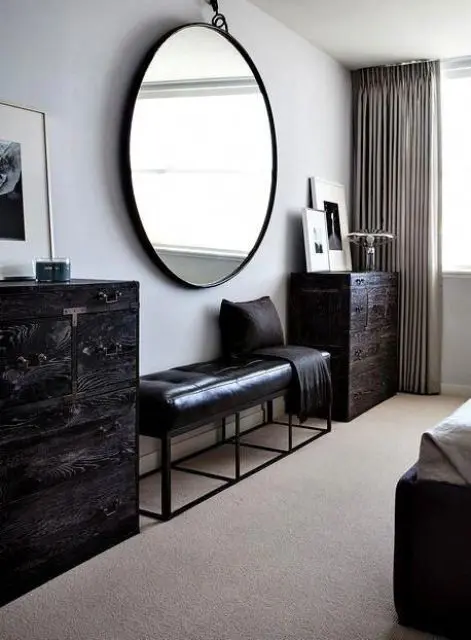 Minimalist bedroom with large round mirror and black furniture.