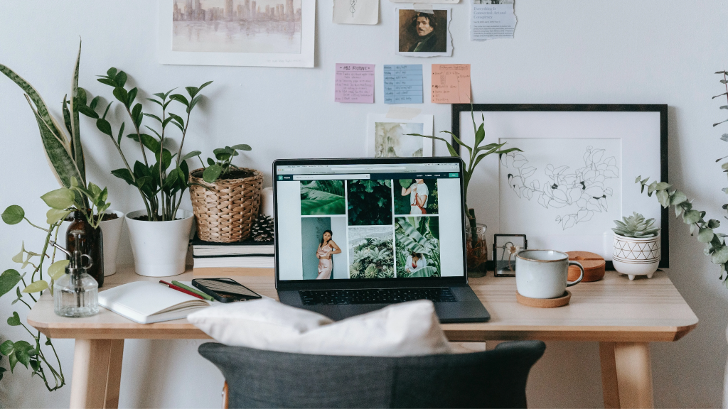 Home office desk filled with potted plants and laptop against inspiration wall.