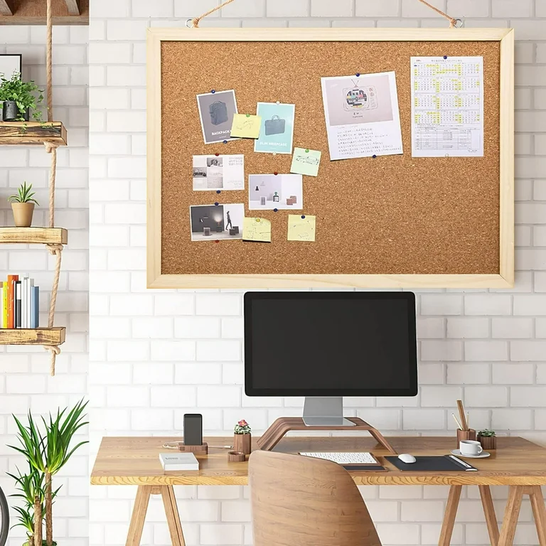 Cork bulletin board above wooden desk with computer and floating shelves.