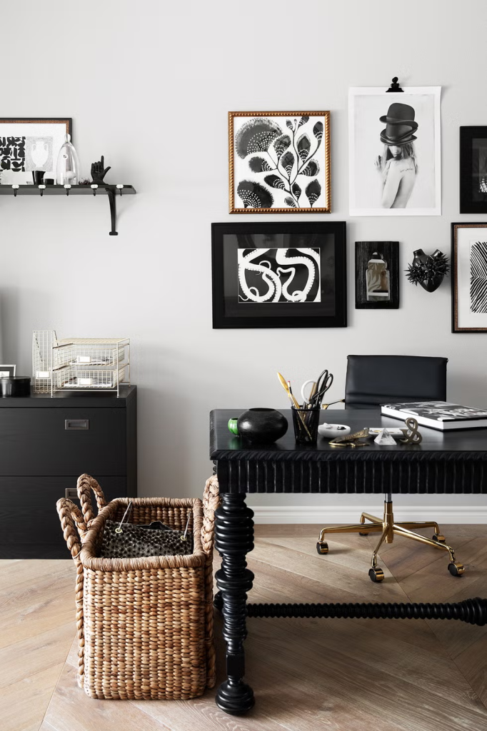 Black desk with intricate legs, wicker basket, modern decor, and monochrome framed art on the wall in a stylish home office.