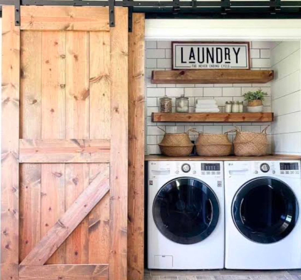 Compact laundry area with sliding barn door and wood shelves holding storage baskets.