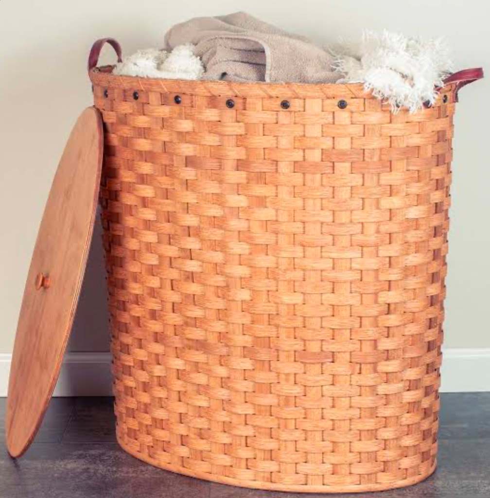 Woven laundry hamper with lid and towels inside.