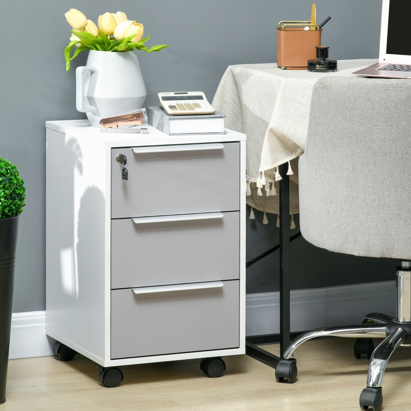 White mobile filing cabinet with three drawers and lock placed beside a desk in a modern workspace.