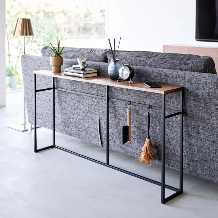 Slim console table with a black metal frame and wooden top placed behind a grey sofa with books and decor.