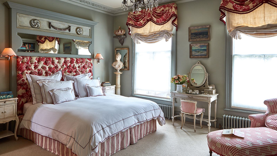 Traditional bedroom with red toile headboard, patterned valances, and vintage vanity in sage room.