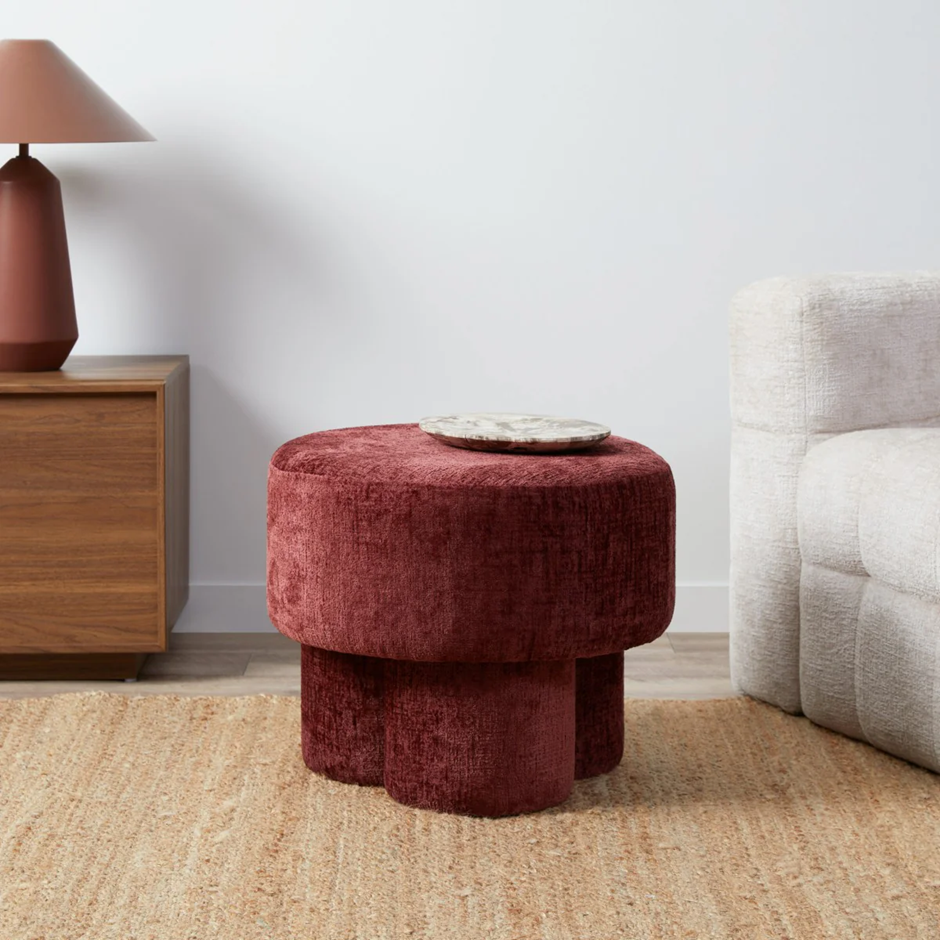 Modern burgundy ottoman with marble top in a minimalist living room with neutral furniture and warm rug