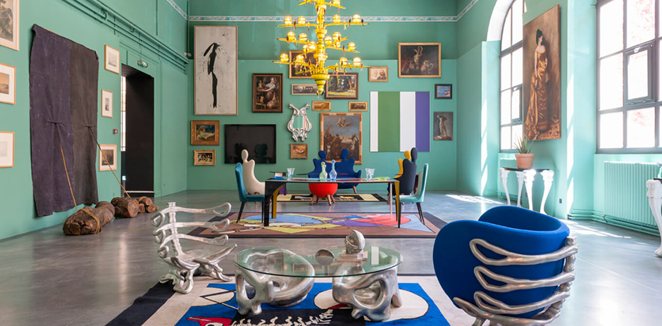 Surrealist interior gallery with teal walls, eclectic art, sculptural chairs, and gold chandelier.