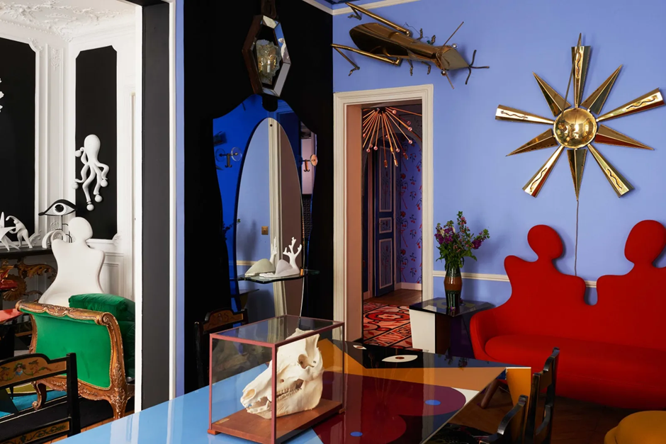 Bold surrealist living room with red sculptural sofa, sunburst wall art, and quirky decor.