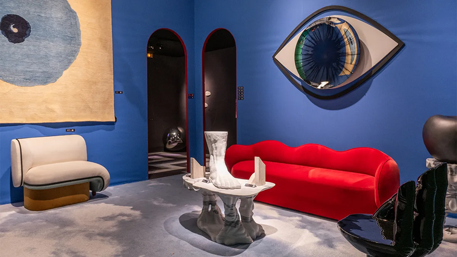 Blue surrealist lounge featuring a red lips sofa and giant eye mirror.