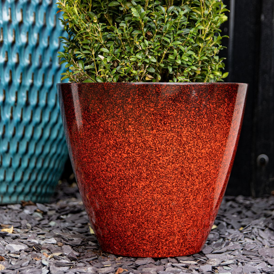 Glossy red-speckled planter with green shrub, adding a bold outdoor accent.