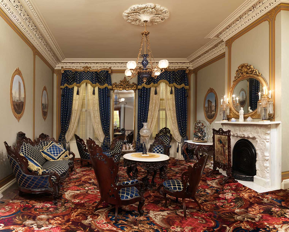 Victorian parlor with blue-and-gold drapes, marble fireplace, carved sofas.