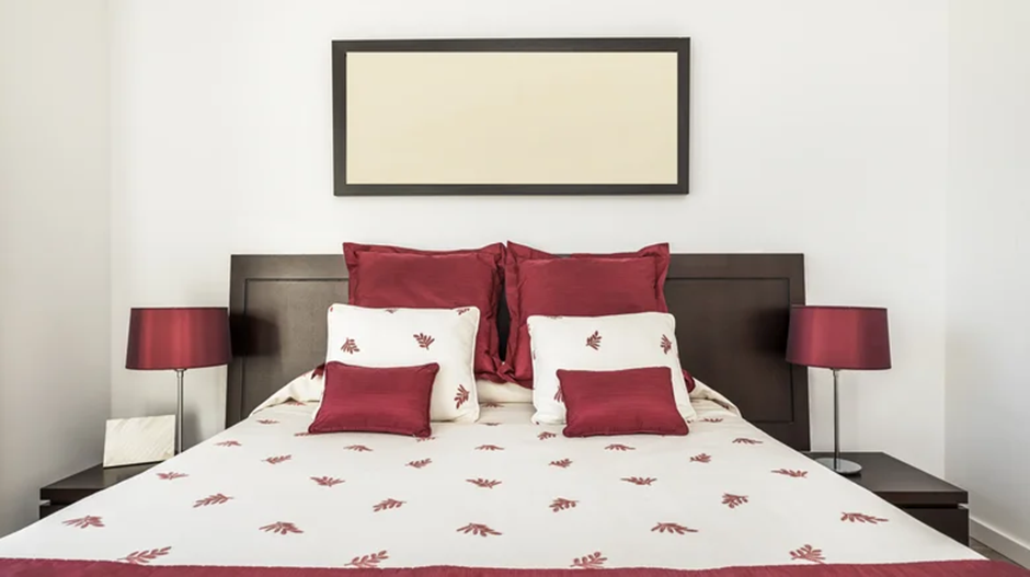 Dark wood bed with red and white bedding, matching red lamps for a warm look.