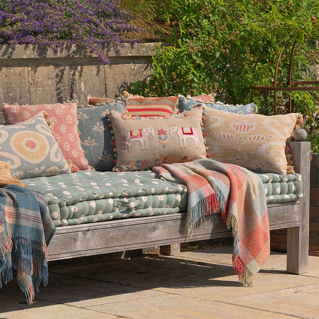 A cozy rustic outdoor bench decorated with colorful cushions and throws.