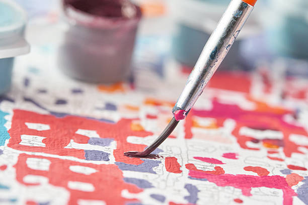 Close up of paintbrush on colorful paint by numbers canvas with blurred paint pots in background.