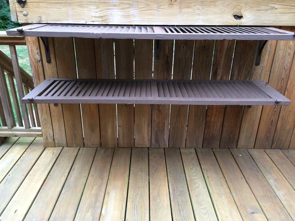 Outdoor wall-mounted shelves made from repurposed brown shutters attached to wooden deck railing, used as rustic storage or display space