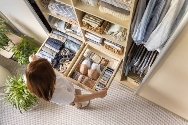Ceiling down view of a woman putting away under garment in a sectioned drawer.