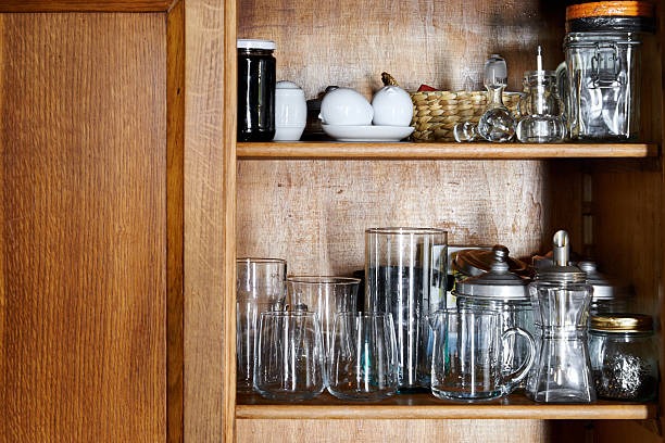 Open wooden cabinet with glass jars, mugs, and neatly arranged kitchen storage items