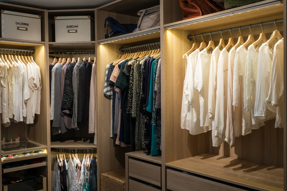 Modern walk-in closet with wooden shelves, hanging rods, drawers, and built-in LED lighting